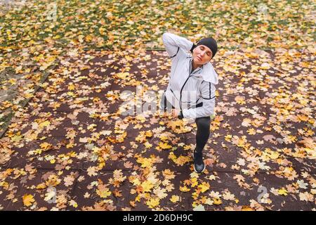 Faites de l'exercice à une femme athlétique avant de faire du jogging dans le parc municipal d'automne sur l'aire de jeux pour enfants. Jeune femme de fitness s'étirant les jambes pendant que wa Banque D'Images