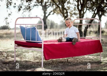 Petit garçon mignon assis sur un lit extérieur parmi des arbres en liège Banque D'Images