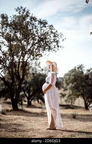 Femme enceinte portant un chapeau et une robe blanche parmi les liège Banque D'Images