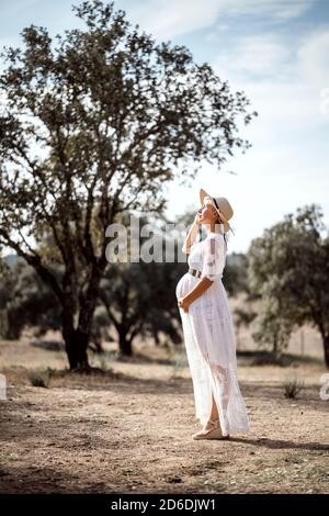 Femme enceinte portant un chapeau et une robe blanche parmi les liège Banque D'Images