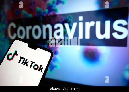 Le logo TikTok affiché sur un téléphone portable avec un modèle d'illustration du coronavirus affiché sur un moniteur en arrière-plan. Banque D'Images