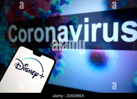 Le logo Disney+ affiché sur un téléphone mobile avec un modèle d'illustration du coronavirus affiché sur un moniteur en arrière-plan. Banque D'Images