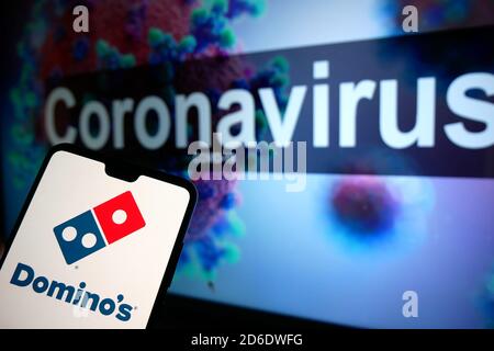 Le logo Domino affiché sur un téléphone portable avec un modèle d'illustration du coronavirus affiché sur un moniteur en arrière-plan. Banque D'Images