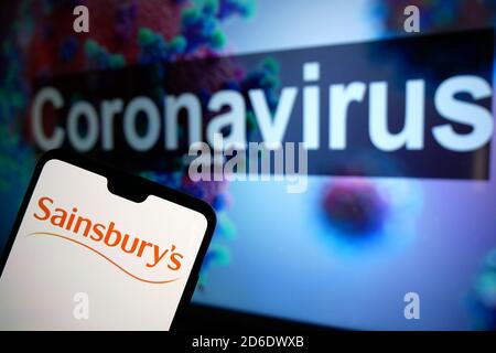 Le logo Sainsburys est affiché sur un téléphone portable avec un modèle d'illustration du coronavirus affiché sur un moniteur en arrière-plan. Photo cre Banque D'Images