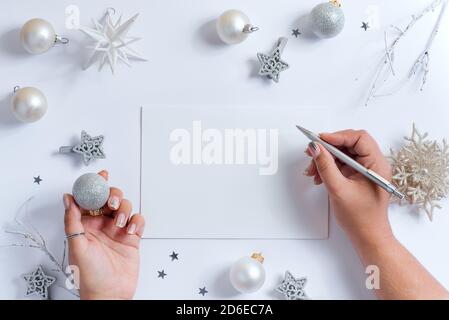 Les mains des femmes écrivent la lettre au Père Noël au-dessus du fond de Noël décoré avec de belles étoiles brillantes et des boules de couleurs blanc et argent, copie Banque D'Images