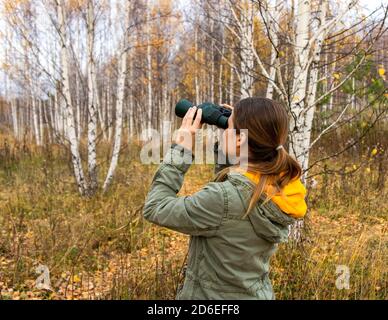 Jeune femme ornithologue avec des jumelles dans la forêt d'automne. Observation des oiseaux, zoologie, écologie. Recherche, observation des animaux. Ornithologie Banque D'Images