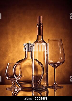 Bouteille de cognac vide, verre de cognac, bouteille de vin et verre de vin sur une surface réfléchissante sur fond de grunge Banque D'Images