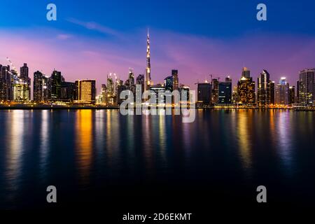 Vue imprenable sur les gratte-ciel illuminés de Dubaï au crépuscule avec le magnifique Burj Khalifa réfléchi sur le canal d'eau qui coule en premier plan. Banque D'Images