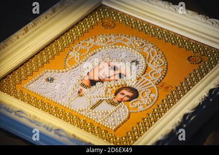 Religion orthodoxe encadrée décorée image brodée. La Vierge Marie et le bébé Jésus en perles blanches sur fond orange. Cadre blanc avec ornements. Main Banque D'Images