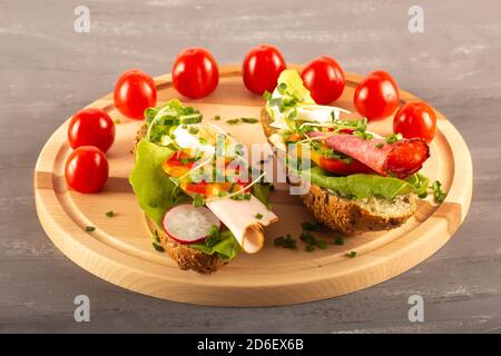 Sandwichs avec légumes, jambon, tomates, œuf sur une table en bois et fond gris. Tomates en arrière-plan. Banque D'Images