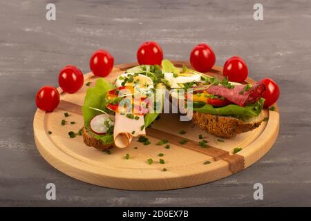 Sandwichs avec légumes, jambon, tomates, œuf sur une table en bois et fond gris. Tomates en arrière-plan. Banque D'Images