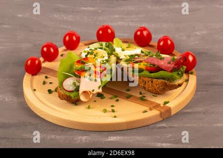 Sandwichs avec légumes, jambon, tomates, œuf sur une table en bois et fond gris. Tomates en arrière-plan. Banque D'Images