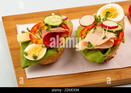 Sandwichs avec légumes, jambon, tomates, œufs sur une table en bois et un fond clair. Tomates en arrière-plan. Banque D'Images