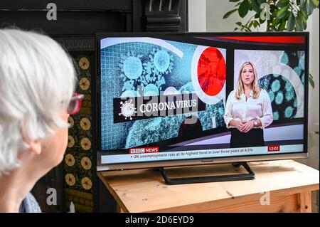 Une femme plus âgée regarde un reportage sur le coronavirus avec un texte sur la hausse du chômage pendant la pandémie. Banque D'Images