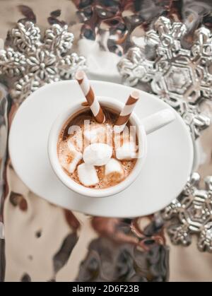 Photo en hauteur d'une tasse blanche de chocolat chaud avec mini-guimauves et pailles à boire rayées sur un plateau argenté Banque D'Images