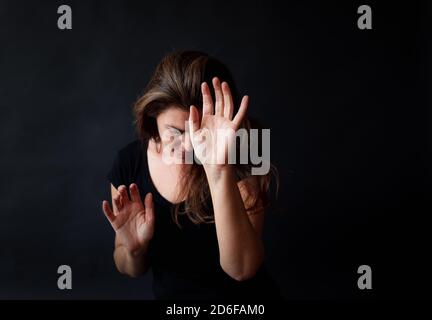 Femme aux longs cheveux bruns atteignant ses mains dans une pièce sombre. Banque D'Images