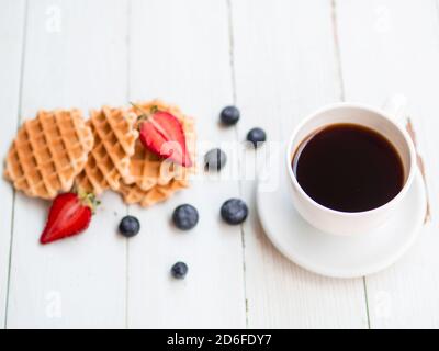 Petit déjeuner sain et délicieux tôt le matin. Gaufres fraîches, myrtilles, fraises, café chaud isolé sur fond de bois blanc ancien. Banque D'Images