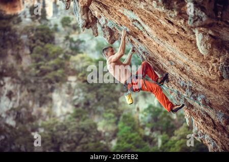 Jeune homme grimpeur sur le mur suspendu. Escalade sur une falaise naturelle. Un jeune homme fort se débat sur un parcours difficile. Banque D'Images