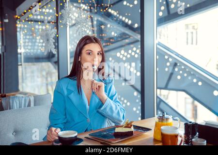 Femme de lécher la cuillère de manger quelque chose de délicieux dans un restaurant chaleureux et des saveurs de la cuisine locale. Hispanic girl wearing costume bleu officiel assis à un tabl Banque D'Images