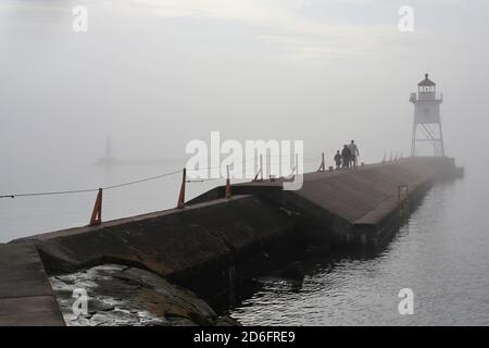 Une famille de trois personnes se promornant le long d'un sentier menant à un phare dans le brouillard, à Grand Marais, Minnesota. Banque D'Images