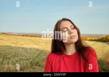 Jeune belle fille dans une robe rouge se tient dans un champ d'automne Banque D'Images