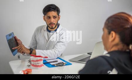 Jeune dentiste hispanique expliquant le problème sur une radiographie à un patient Banque D'Images