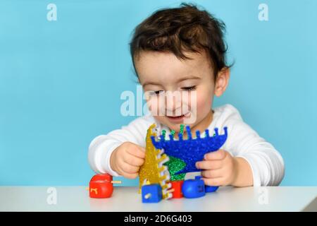 Un garçon juif joue avec la menorah bleue festive Hanukkah et les Dreidels en bois colorés. Mise au point sélective. Banque D'Images