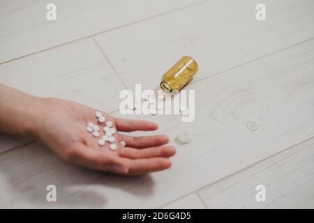 Gros plan de la main avec une poignée de pilules dans la paume, couché sans vie sur le sol. Une bouteille de pilules se trouve à proximité. Les conséquences de la dépression, su Banque D'Images