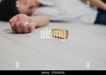 Au premier plan, la main avec une poignée de pilules dans la paume est sans vie sur le sol. Une bouteille de pilules se trouve à proximité. Sur l'arrière-plan du Banque D'Images