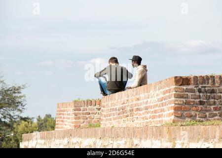 Belgrade, Serbie - 09 octobre 2020 : deux jeunes hommes assis sur le haut de la forteresse de Kalemegdan mur de briques par une journée ensoleillée, de l'arrière Banque D'Images