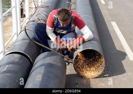 Belgrade, Serbie - 09 octobre 2020 : soudeur coupant un tube de tuyau métallique large avec une torche de coupe oxy-fuel, avec flamme et étincelles, à l'extérieur sur la rive Banque D'Images