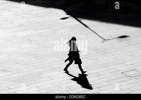 Belgrade, Serbie - 09 octobre 2020 : silhouette d'ombre d'une jeune femme marchant sur la chaussée carrée de la ville, en vue à grand angle noir et blanc Banque D'Images