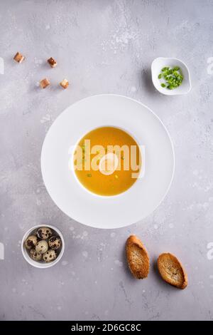 Bouillon dans une assiette à soupe blanche, oignons ou oignons verts hachés, œufs de caille, pain grillé et croûtons sur fond gris. Pose à plat. Orientation verticale Banque D'Images