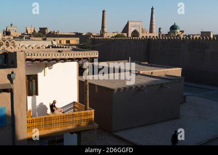 Une femme touriste de l'Ouest lisant un livre sur un balcon éclairé au soleil près de l'Itchan Kala, la ville intérieure fortifiée de Khiva, en Ouzbékistan. Banque D'Images