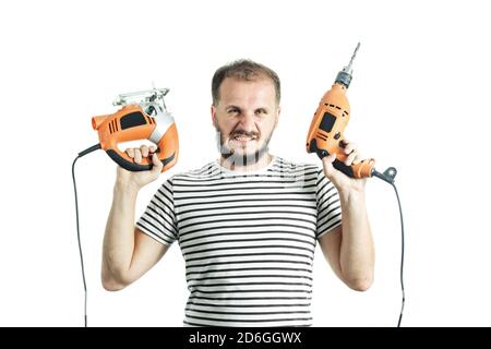 Un grin dans un T-shirt rayé, tient une perceuse et une scie électrique dans ses mains. Isolé sur fond blanc Banque D'Images