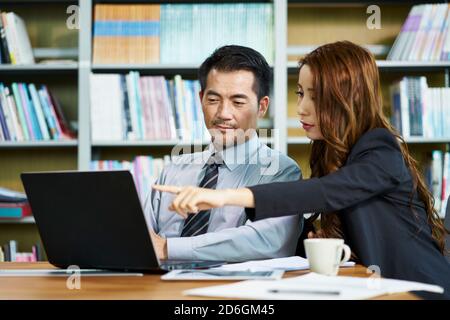 homme d'affaires et femme d'affaires asiatiques ayant une discussion dans le bureau avec ordinateur portable Banque D'Images