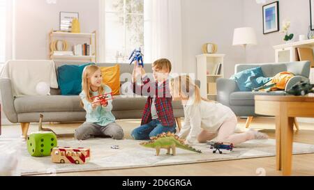 Dans le salon: Garçon et fille jouant avec les avions et les dinosaures tout en étant assis sur un tapis. Salon ensoleillé avec enfants s'amuser. Banque D'Images