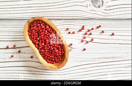 Grains de poivre rouge ou rose dans un petit bol en bois, certains éparpillés sur le bureau de tableaux blancs, photo de gros plan du dessus Banque D'Images