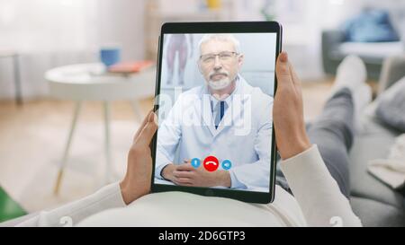 Jeune fille à la maison utilisant une tablette numérique pour parler à son docteur via Video Conference Medical App Woman vérifie les symptômes possibles avec Professional Banque D'Images