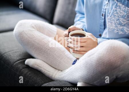Longues chaussettes chaudes et douillettes et une tasse de thé chaude en hiver. Femme appréciant un style de vie détendu sur un canapé à la maison. Personne malade avec la grippe ou la fièvre assis sur le canapé. Banque D'Images