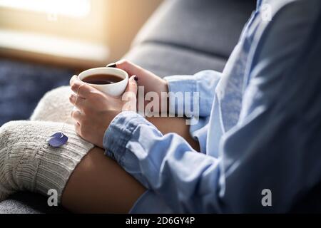 Confort matinal d'hiver froid à la maison avec thé chaud. Bonne femme tenant une tasse chaude. Personne malade avec la grippe ou la fièvre. Détendez-vous sur un canapé confortable. Banque D'Images