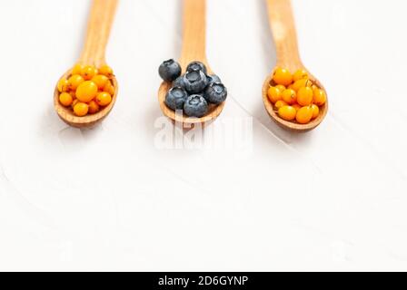 Bleuets mûrs et baies d'argousier en cuillères en bois sur fond blanc. Copier l'espace, la pose à plat, placer pour le texte. Dessert naturel, sain snac Banque D'Images