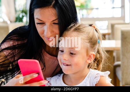 Une fille souriante prend un selfie avec une jolie fille sur un smartphone, une jeune mère heureuse rit, prend une photo avec sa petite fille, jouant du plaisir avec le TH Banque D'Images