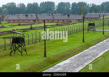 Une section du musée d'État d'Auschwitz-Birkenau à Oswiecim en Pologne montrant la clôture électrique et les cheminées de briques des casernes de prisonniers. Banque D'Images