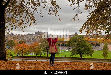 Inverleith Park, Édimbourg, Écosse, Royaume-Uni. 17 octobre 2020. Lors d'une journée de découverte, les arbres commencent à perdre leurs couleurs d'automne à Inverleith avec le centre-ville en arrière-plan. Une dame prend un photogaphe avec son téléphone portable. Crédit : Arch White/Alamy Live News Banque D'Images