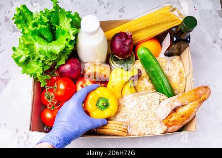 Faites du bénévolat en portant des gants pour donner de la nourriture dans une boîte en carton contenant divers aliments. Ouvrir la boîte en carton contenant de l'huile, des légumes, du lait, des conserves, des céréales et Banque D'Images