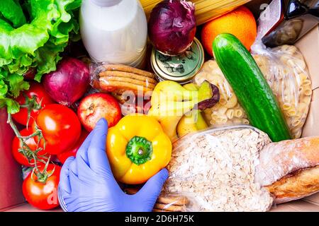 Faites du bénévolat en portant des gants pour donner de la nourriture dans une boîte en carton contenant divers aliments. Ouvrir la boîte en carton contenant de l'huile, des légumes, du lait, des conserves, des céréales et Banque D'Images