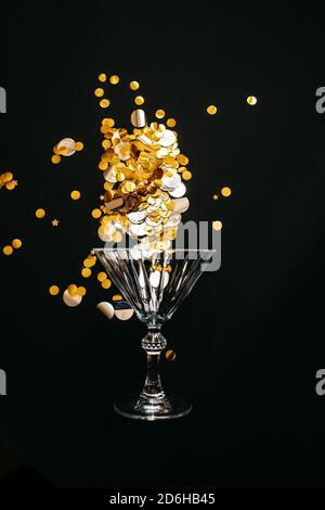 Verre à vin avec des sparkles d'or ou confetti sur fond noir. Concept de célébration. Banque D'Images