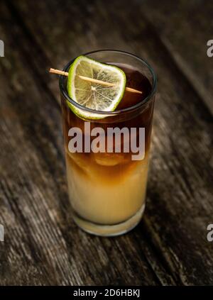Cocktail sombre et orageux dans un verre à boule haute avec de la glace et une garniture de citron vert sur une vieille table en bois avec un fond noir Banque D'Images