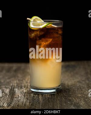 Cocktail sombre et orageux dans un verre à boule haute avec de la glace et une garniture de citron vert sur une vieille table en bois avec un fond noir Banque D'Images